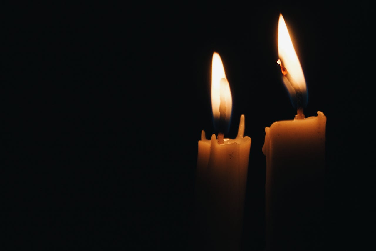 Close-up of two burning candles illuminating the dark ambiance.