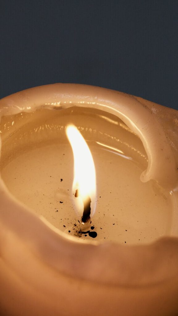 Close-up view of a lit candle with wax drips and a glowing flame against a dark background.