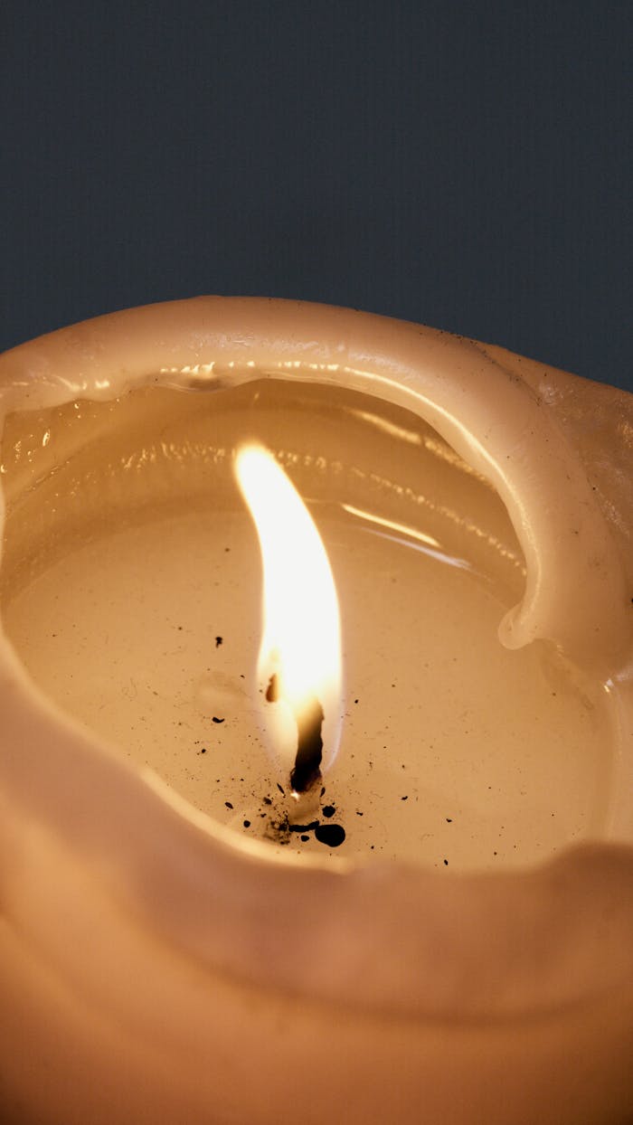 Close-up view of a lit candle with wax drips and a glowing flame against a dark background.
